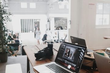 A bright, modern workspace featuring laptops, a camera, and a drawing tablet in an indoor office.